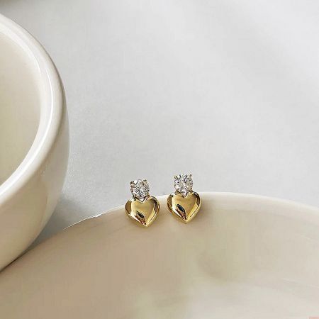 The gold heart earrings with gemstones displayed on a white ceramic surface.