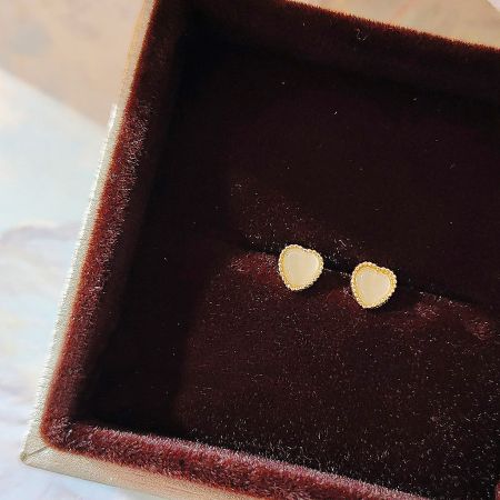 Gold heart earrings with white stones displayed in a luxurious red velvet box.