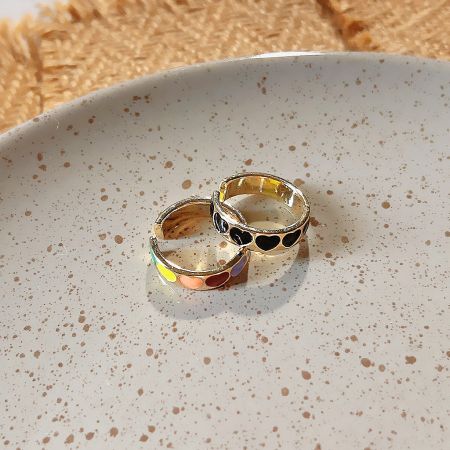 Two gold heart-shaped enamel rings from the set displayed on a decorative plate.