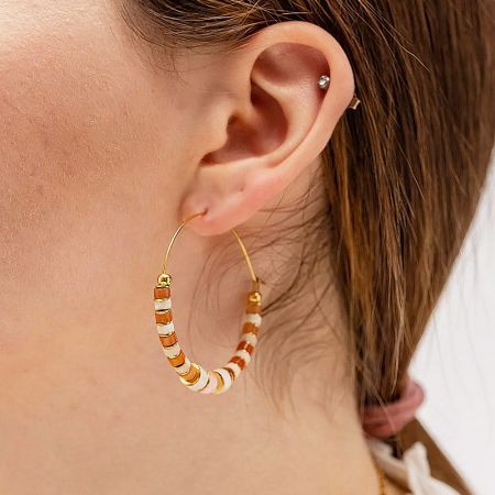 Model wearing a gold hoop earring with white, orange, and gold beads to showcase its size and style.