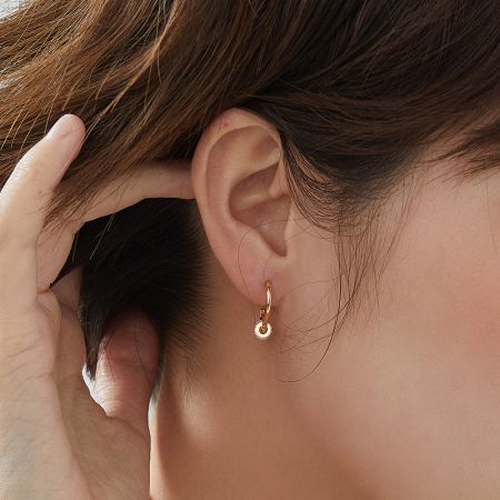 A woman wearing the elegant gold hoop earring with its circular charm.