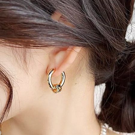 Close-up view of a gold-plated huggie hoop earring being worn.