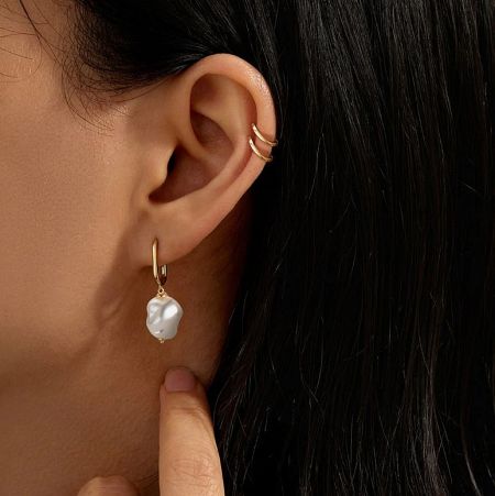 Close-up of a single gold hoop earring with a large, unique baroque pearl, highlighting its natural, irregular shape.