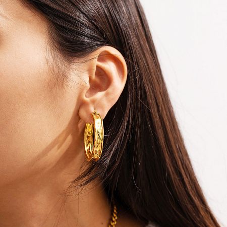 Model wearing the PVD gold hammered hoop earrings to show scale and style.