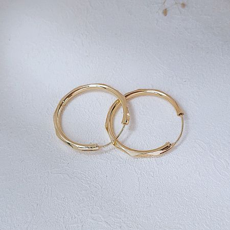 A pair of 28mm gold infinity hoop earrings presented for wholesale.