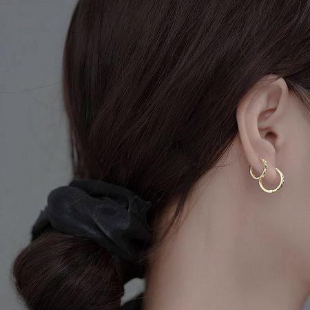 Detailed view of a pair of gold huggie hoop earrings being worn, highlighting their shine.