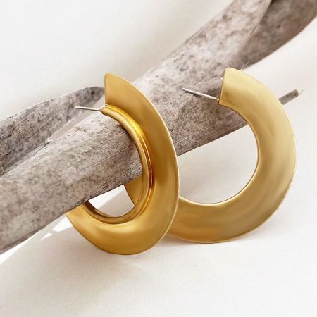 A pair of gold geometric C hoop earrings displayed on a piece of driftwood for an artistic presentation.