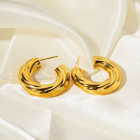 Close-up of the gold twisted hoop earrings resting on a luxurious satin background.
