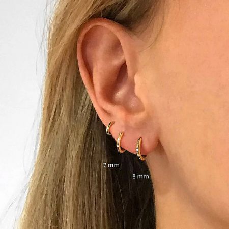 Model wearing two different sizes of gold hoop cartilage earrings for size comparison.