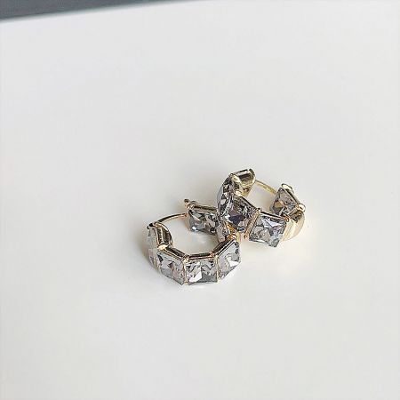 Detailed shot of gold hoop earrings with a hexagonal pattern of clear gemstones.