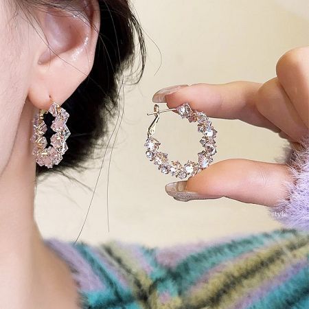 A hand holding the gold hoop earring to display its craftsmanship and detail.