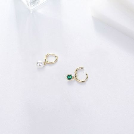 Full view of the asymmetrical pearl and emerald huggie hoops on a white background.