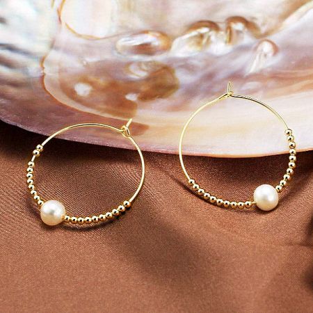 Product shot of the gold pearl hoop earrings styled on a textured brown fabric next to a seashell.