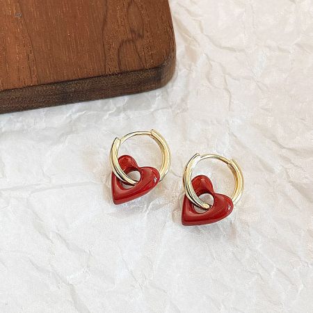 Gold hoop earrings with red heart charms displayed on a white surface.