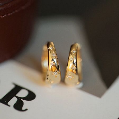 A pair of gold hoop earrings with a star and zirconia design against a neutral background.