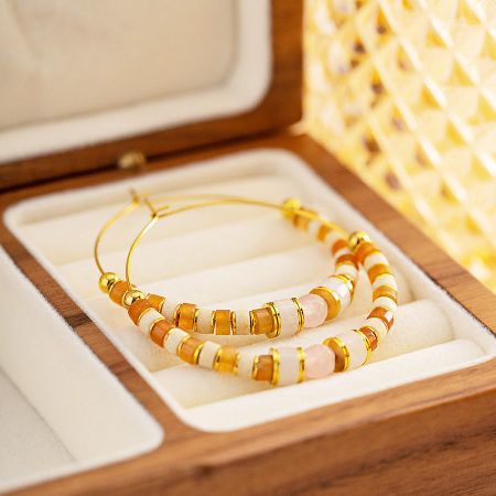 Stylish gold hoop earrings with white, orange, and gold beads elegantly displayed in a jewelry box.