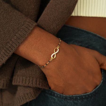 A detailed view of the gold infinity symbol bracelet, emphasizing the brilliant white zircon stones.