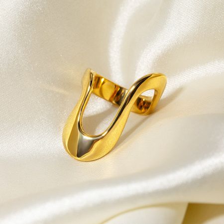 Detailed view of the gold infinity symbol ring from the geometric set on a white satin background.