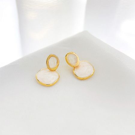 Close-up view of the gold-plated drop earrings, highlighting the iridescent quality of the cream-white enamel.