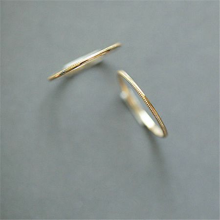 A pair of minimalist gold rings from the stackable set displayed on a neutral gray background.