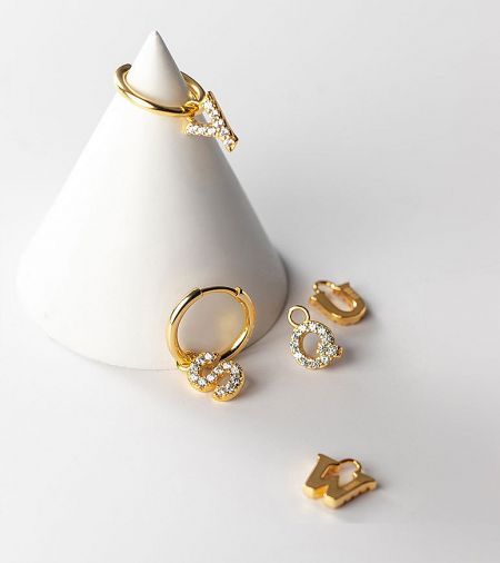 A display of various gold initial jewelry pieces, including hoop earrings and charms with diamonds.
