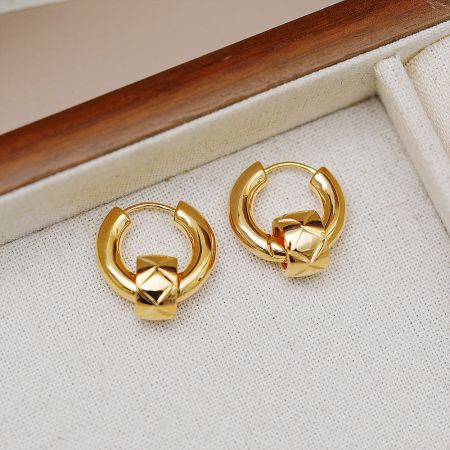A pair of gold knot design huggie earrings in a wooden box.