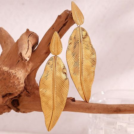 A pair of gold leaf earrings displayed on a piece of driftwood.