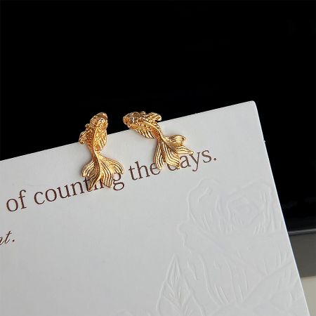 Close-up of the matte gold Koi Fish stud earrings presented on a display card, highlighting their detailed craftsmanship.