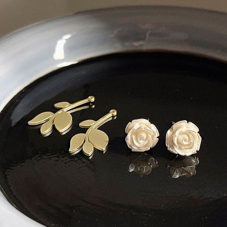 A comparison image showing the white rose stud earrings alongside a pair of gold leaf-shaped earrings.
