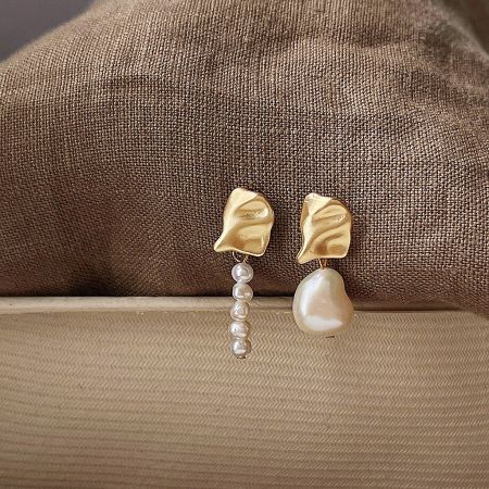 Detailed shot of gold leaf-shaped earrings with white pearl drops on a fabric surface.