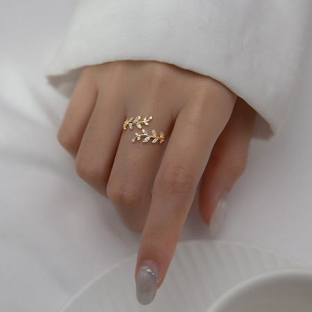 Close-up of the gold-plated leaf ring on a woman's hand, showing the sparkling clear gemstones.