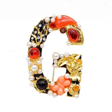 Detailed view of the gold-toned letter 'G' brooch, adorned with vibrant gemstones and classic pearls.