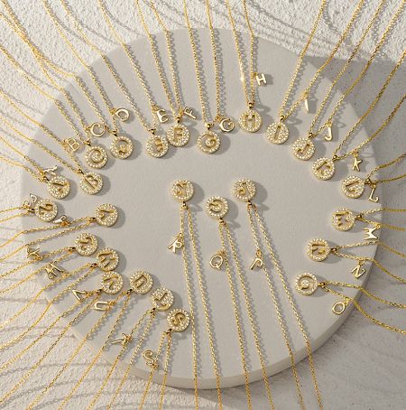 A collection of gold-plated initial coin necklaces with various letters.