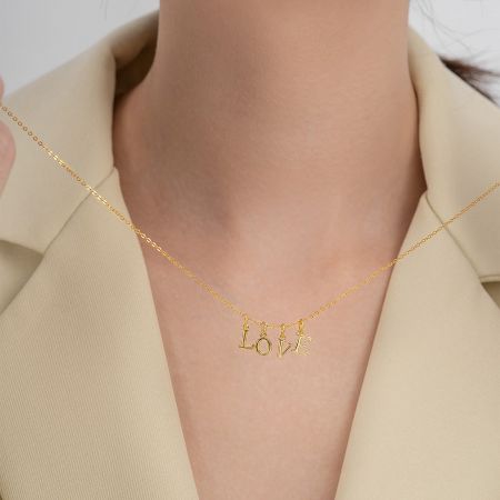 A model wearing a custom gold necklace spelling 'LOVE' with alphabet pendants.