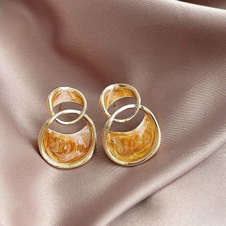 Detailed view of the double-loop stud earrings, showing the shiny gold finish and marbled enamel in shades of camel, white, and yellow.