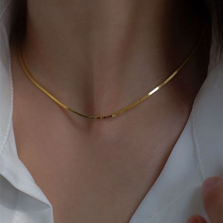 Close-up of the gold herringbone snake chain necklace worn on a model's neck.