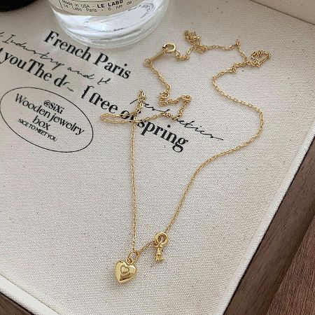 Detailed view of the gold heart key pendant necklace on a textured fabric background.