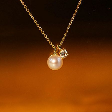 Detailed shot of the pearl and zircon pendant on the gold chain.