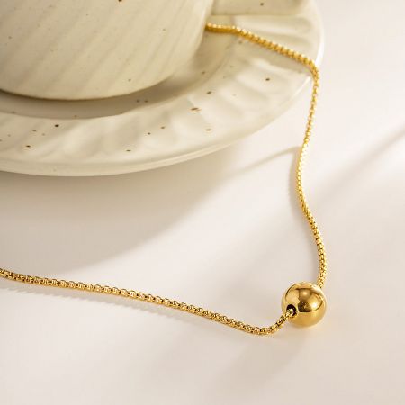 Styled shot of the gold ball pendant necklace next to a white ceramic cup.