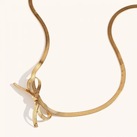 Detailed view of the gold necklace's bow pendant, emphasizing the flat snake chain texture.