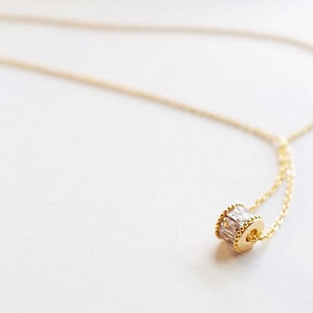 Close-up of a gold choker with a clear baguette-cut gemstone pendant.