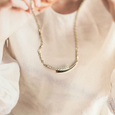 Detailed view of the gold necklace with a curved bar and diamond-studded section.