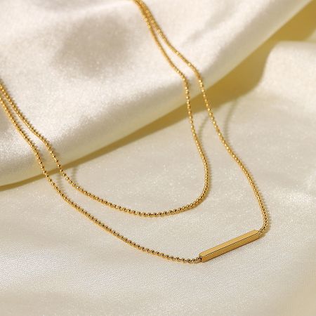 Detailed view of the gold cylindrical bar pendant on the layered necklace.