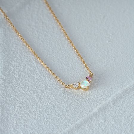 A detailed view of a gold necklace from the set, showcasing an opal, a clear CZ, and a pink gemstone.