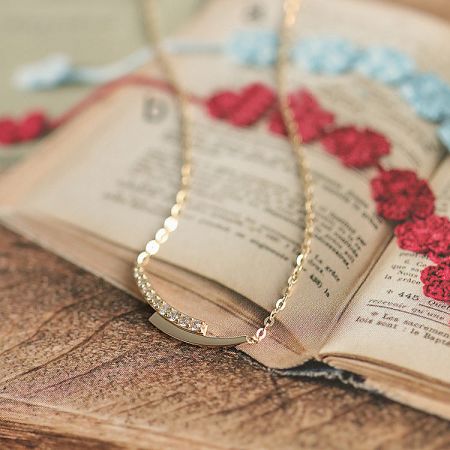 The elegant gold necklace with a diamond pendant displayed on a book.