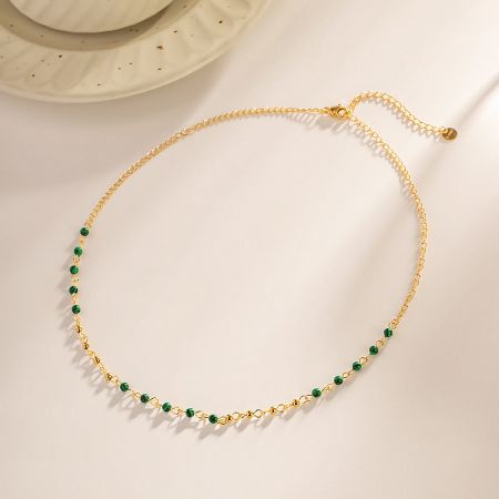 Close-up view of the delicate green beads and gold chain of the stainless steel necklace.