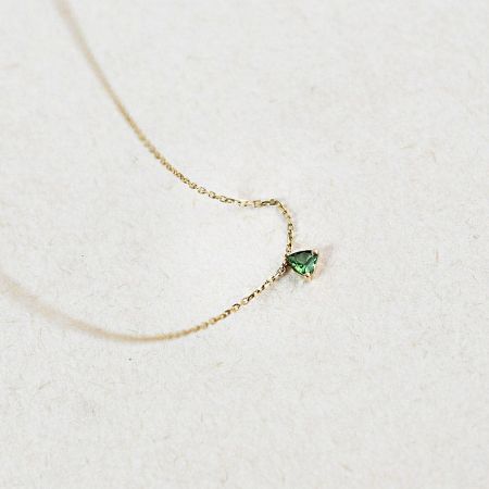 Detailed view of the triangular green emerald stone on the gold necklace.
