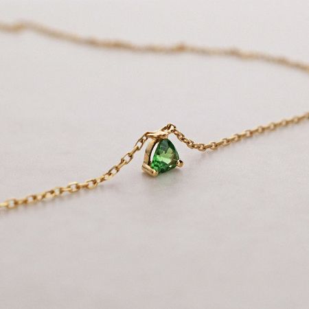 Angled shot of the 18k gold plated necklace with its vibrant green stone.