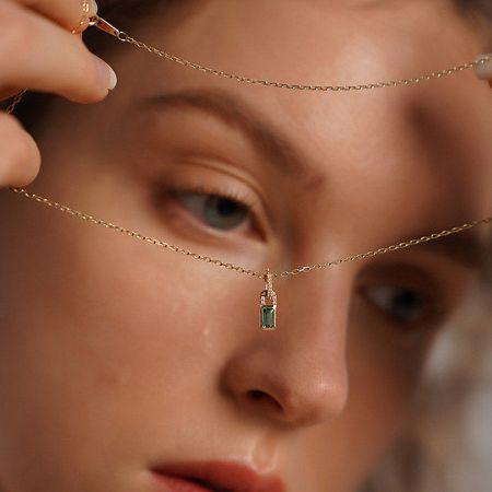 A hand holding the delicate gold-finished necklace, focusing on the green pendant's sparkle.