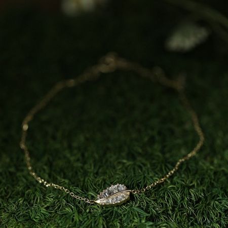 A stunning gold-plated leaf bracelet from the set, displayed on a natural green background to highlight its design.